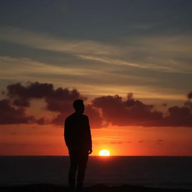 A person silhouetted against a spectacular sunset over the ocean